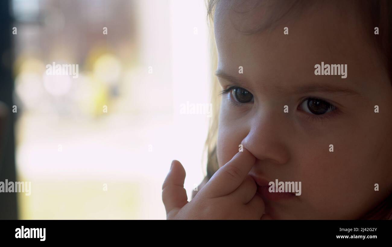 Nahaufnahme kleines Baby in weiß Fütterung bis Hochstuhl, Kind pocht Nase nachdenklich irgendwo suchen. Glückliches Kind mit Nahrung verschmutztes Gesicht. Kleines Mädchen Stockfoto