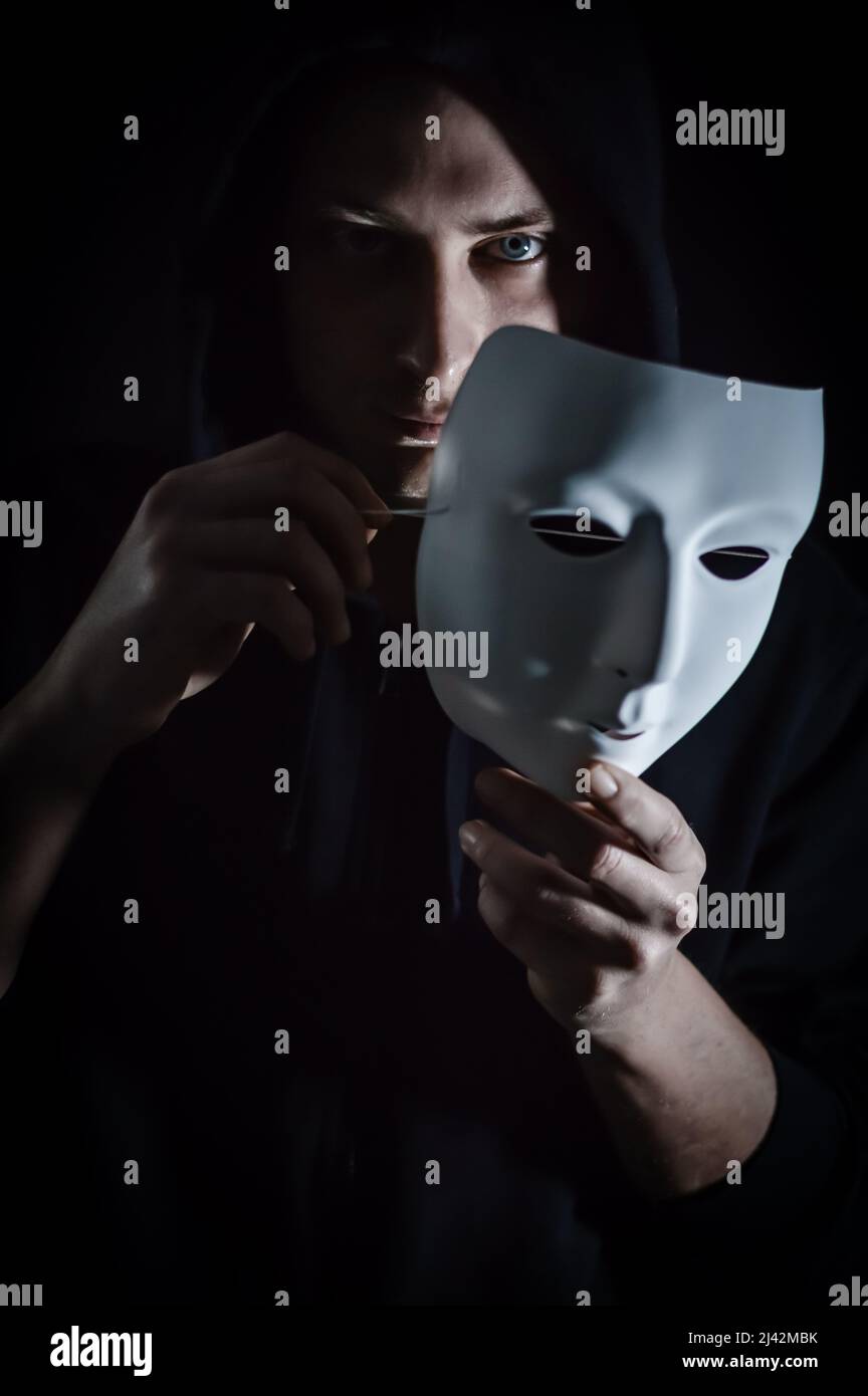 Die Maske ausziehen - Portrait eines jungen Kapuzenmannes, der seine Maske auszieht, seinen Blick sehen lässt, Konzept für wahr und authentisch zu sein Stockfoto