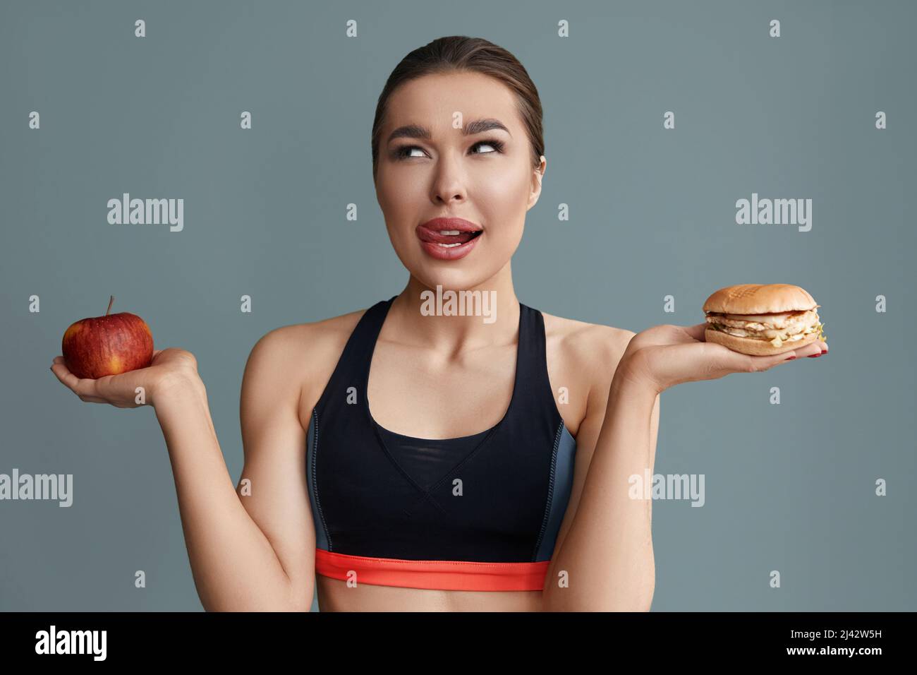 Frau, die zwischen Apfel und Hamburger wählen kann. Diät-Konzept. Gesunde Ernährung, Stockfoto