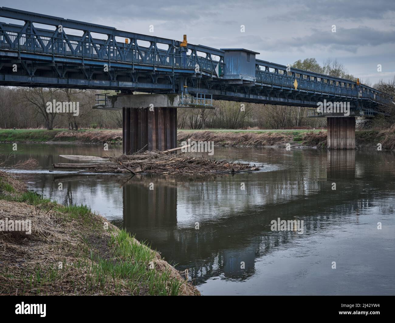 Blaue Metallbrücke über den Fluss Morava mit Treibholz, das auf einer Säule in der Slowakei gefangen wurde. Stockfoto