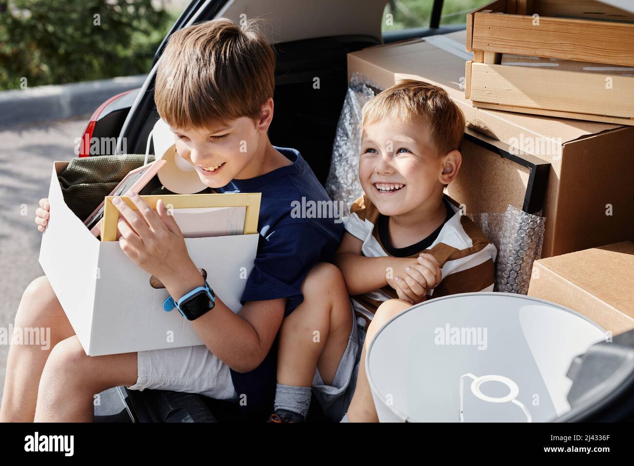 Porträt zweier lächelnder Jungen, die mit Kisten im Kofferraum sitzen und in ein neues Haus ziehen Stockfoto