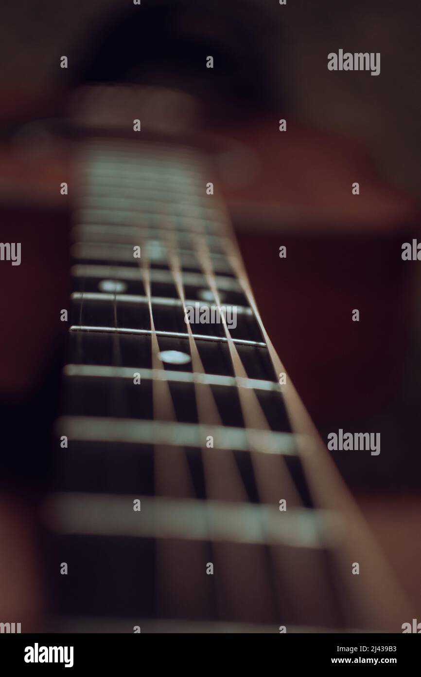 Nahaufnahme Blick auf den Hals einer Gitarre zeigt das Griffbrett mit mehreren Bünden und Positionsmarkierungen mit dem Gitarrenkörper im Hintergrund Stockfoto