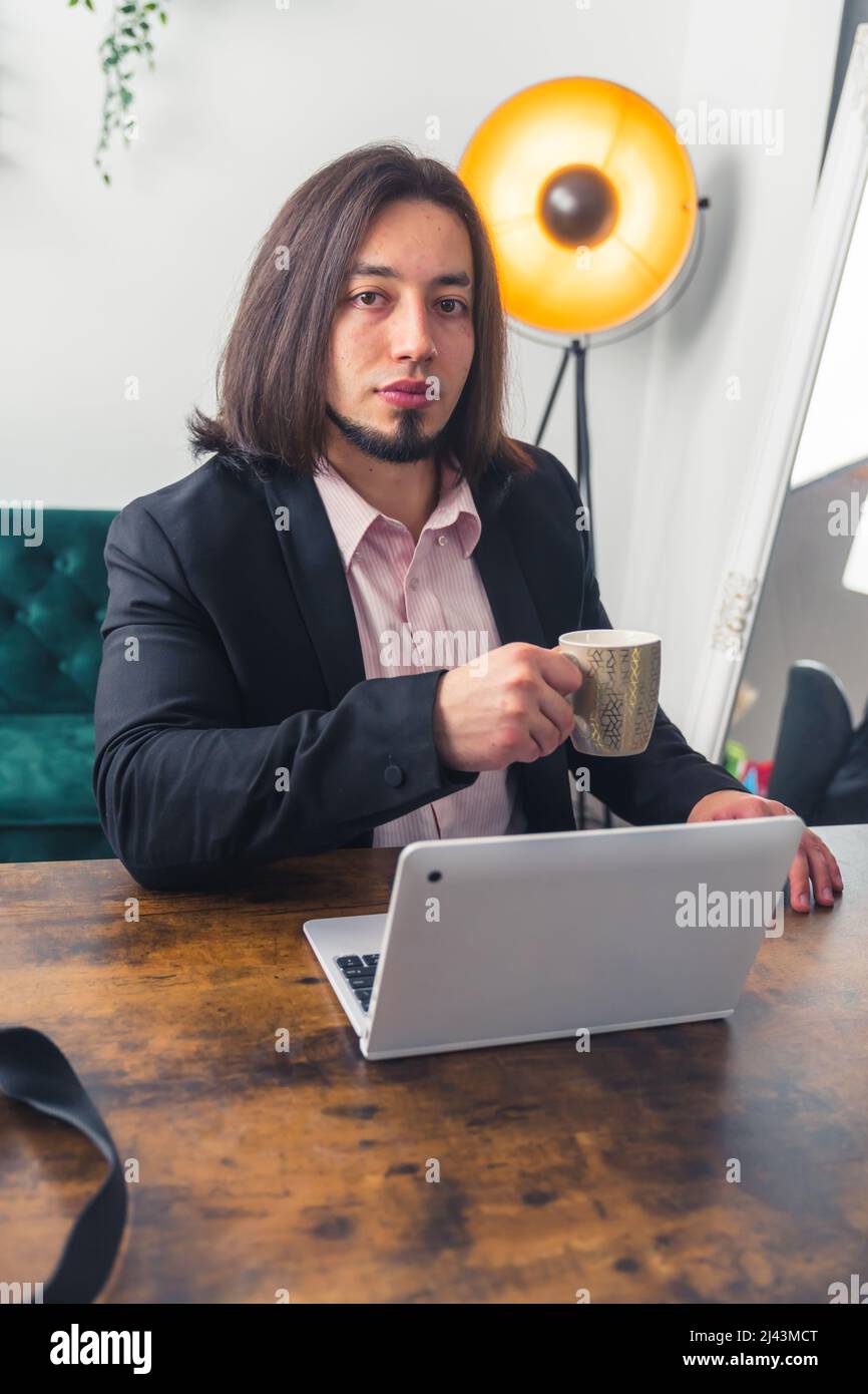 Ein hübscher europäischer Mann arbeitet zu Hause, sitzt vor dem Laptop, mit einem Becher in der Hand Remote Job Concept . Hochwertige Fotos Stockfoto