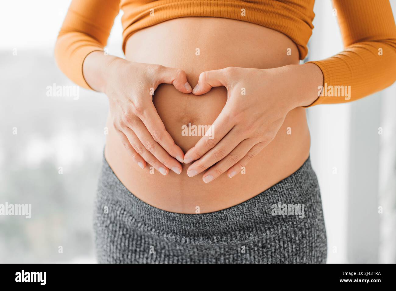 Schwanger Frau hält Magen in Herzform Geste mit den Händen auf ihrem Bauch. Schwangerschaft Konzept Fotoshooting Stockfoto