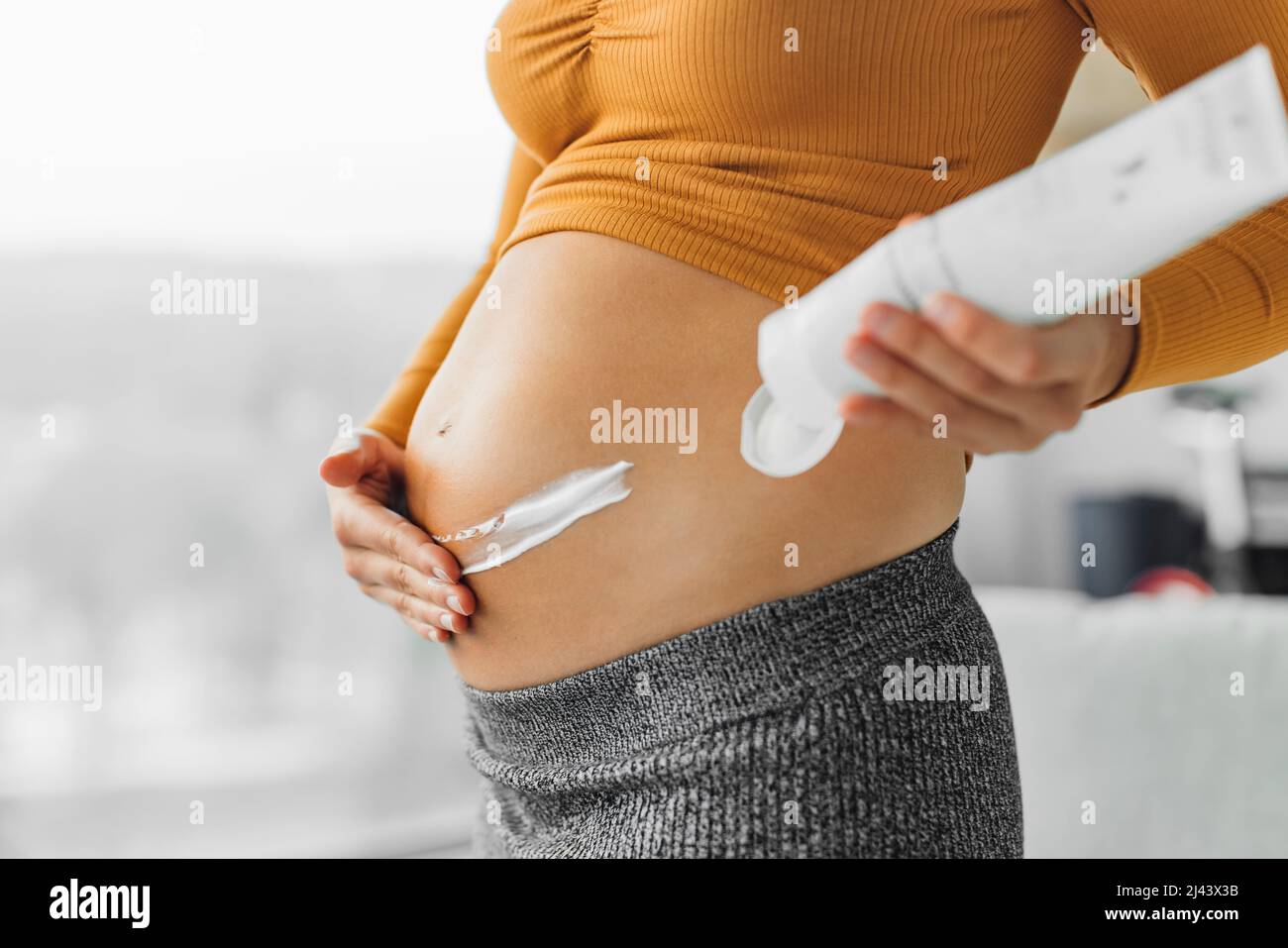 Hautpflege während der Schwangerschaft. Schwangerin, die Creme auf den Bauch für Dehnungsstreifen auftragend. Feuchtigkeitsspendende Nahaufnahme der Hände und Lotion Flasche zu Hause Stockfoto