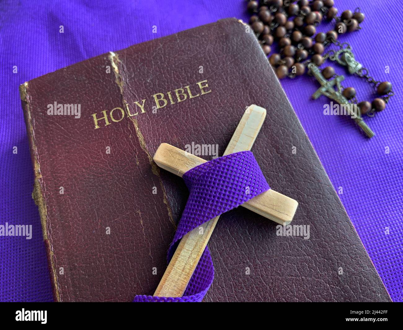 Heiliges Kreuz auf Bibel mit Rosenkranz und lila Deckblatt Hintergrund. Religiöses und kopierraumes Konzept Stockfoto