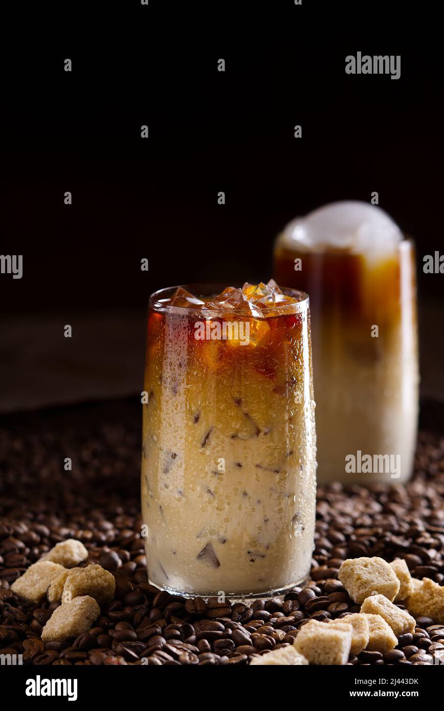 Eiskaffee. Leckerer Eiskaffee mit Milch, kaltes Getränk im Glas mit Eis auf dunklem Kaffeehintergrund. Stockfoto
