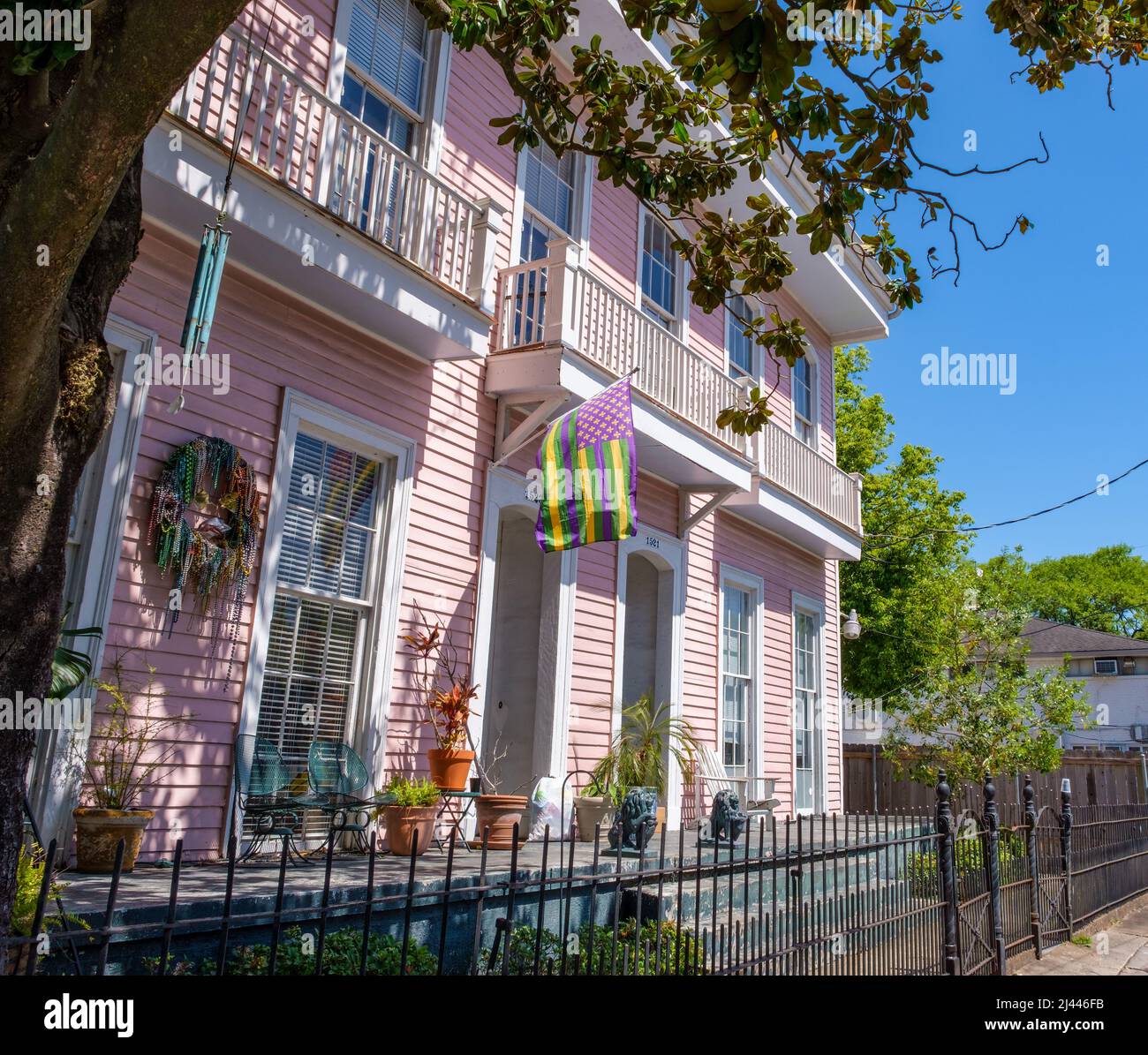 NEW ORLEANS, LA, USA - 10. APRIL 2022: Altes rosafarbenes Apartmentgebäude mit einer Mardi Gras farbigen amerikanischen Flagge und anderen Mardi Gras Dekorationen Stockfoto