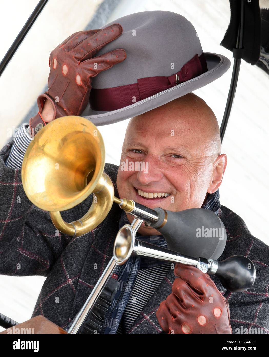 PRODUKTION - 07. April 2022, Sachsen, Leipzig: Der ehemalige Automanager Joe Laube sitzt in seinem E-Wagen 1. in Leipzig, während er die Gäste in einer Tweed-Jacke, einem grauen Melone und zwei Ballhörnern, die für die Verkehrssicherheit notwendig sind, durch das Leipziger Industriegebiet chauffiert. Als Touristenattraktion kann er in seiner komfortablen Kutsche ohne Pferde bis zu sieben Personen unterbringen, denen je nach Wunsch verschiedene Touren zu Sehenswürdigkeiten in der Stadt und Umgebung angeboten werden. Mit einer Höchstgeschwindigkeit von 25 Stundenkilometern und dem leisen Schnurren des Elektromotors können seine Gäste dann die ungewöhnliche Fahrt mit einem Glas genießen Stockfoto PRODUKTION - 07. April 2022, Sachsen, Leipzig: Der ehemalige Automanager Joe Laube sitzt in seinem E-Wagen 1. in Leipzig, während er die Gäste in einer Tweed-Jacke, einem grauen Melone und zwei Ballhörnern, die für die Verkehrssicherheit notwendig sind, durch das Leipziger Industriegebiet chauffiert. Als Touristenattraktion kann er in seiner komfortablen Kutsche ohne Pferde bis zu sieben Personen unterbringen, denen je nach Wunsch verschiedene Touren zu Sehenswürdigkeiten in der Stadt und Umgebung angeboten werden. Mit einer Höchstgeschwindigkeit von 25 Stundenkilometern und dem leisen Schnurren des Elektromotors können seine Gäste dann die ungewöhnliche Fahrt mit einem Glas genießen Stockfoto