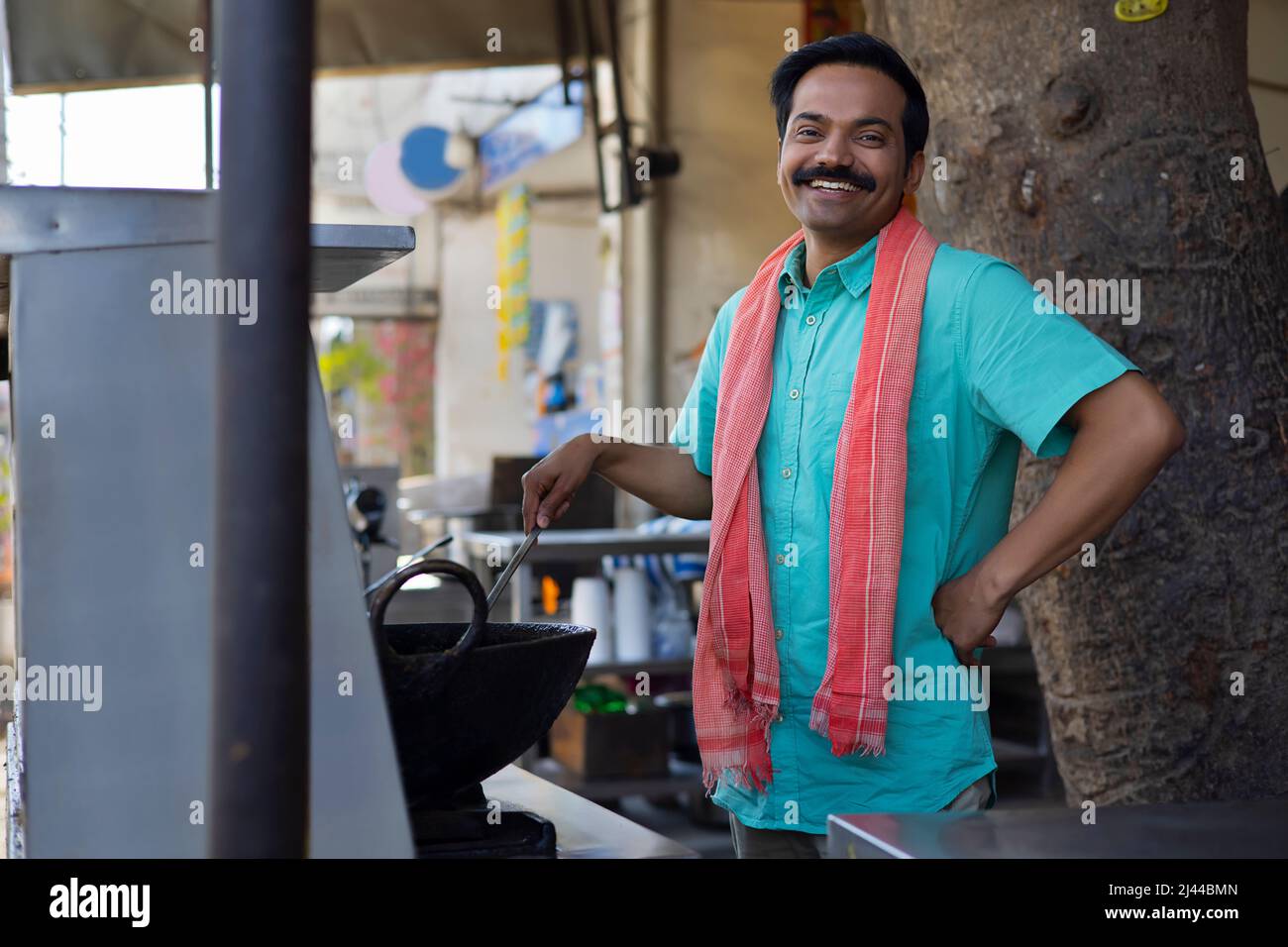 Der Straßenverkäufer schaut lächelnd auf die Kamera, während er an einem Stall Essen macht Stockfoto