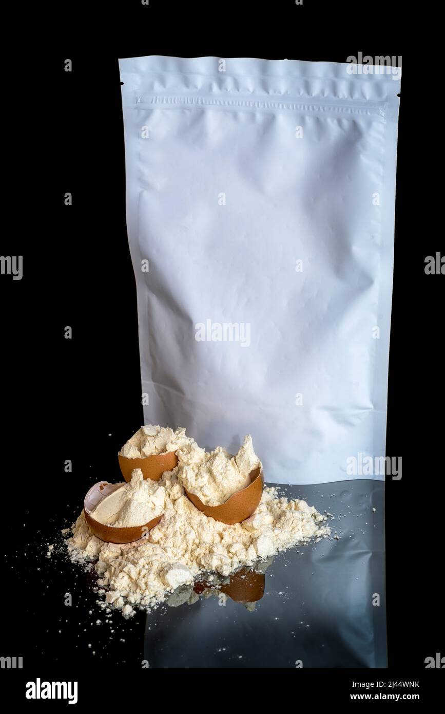 Eiproteinpulverhaufen und Eierschalen, weißes Paket mit Kopierraum, isoliert auf schwarzem Hintergrund mit Spiegelreflexion auf dem Tisch. Sport Stockfoto
