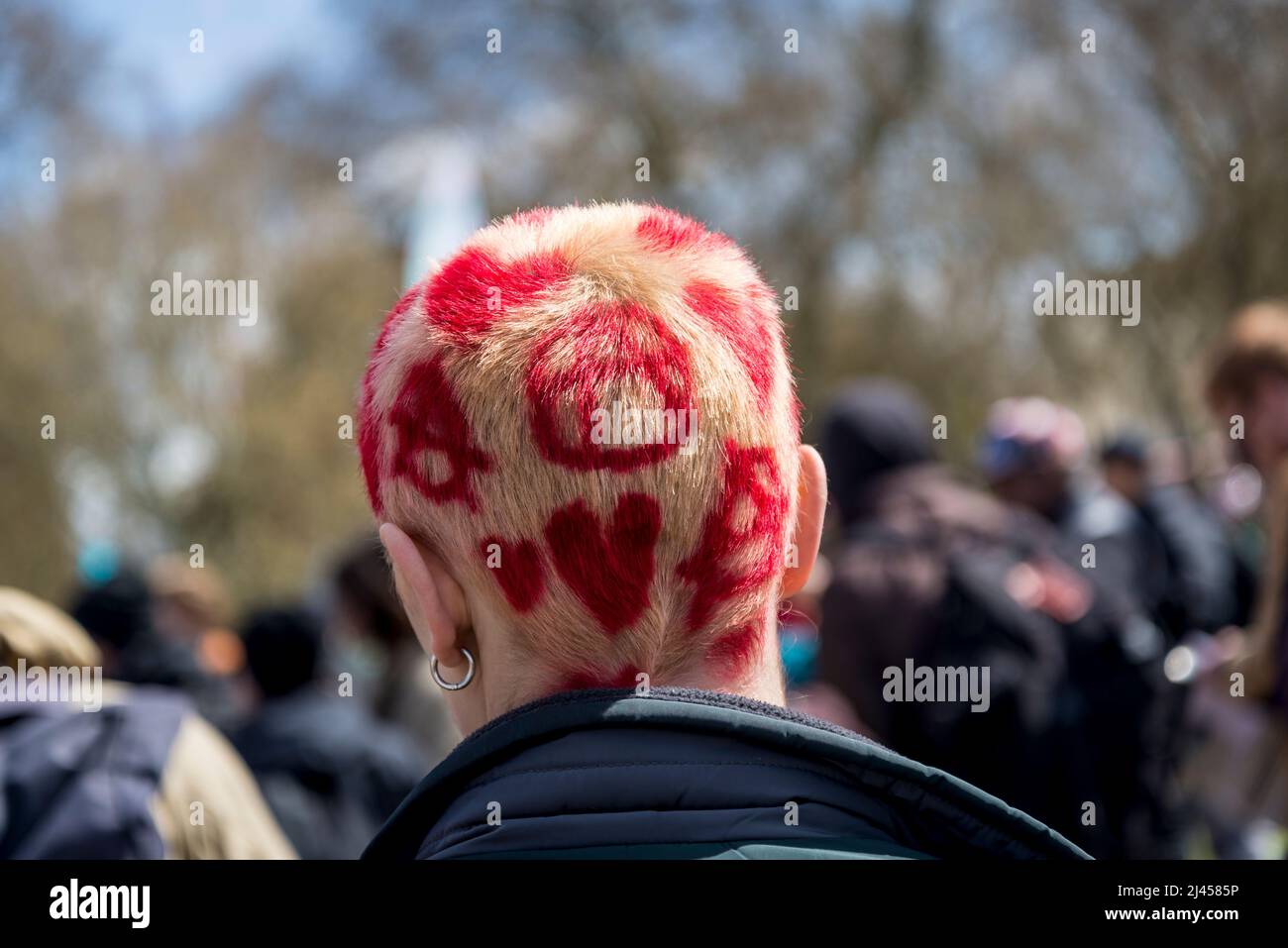 Hinterkopf einer jungen Frau mit gebleichtem Haar und roten Herzen und Anarchesymbolen, bei einem Extinction Rebellion Protest, London, England, Großbritannien Stockfoto