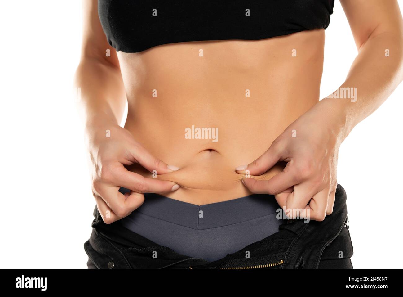 Nahaufnahme einer jungen, fetten Frau, die ihren fettarmen Bauch auf einem weißen Hintergrund kneifen soll. Stockfoto
