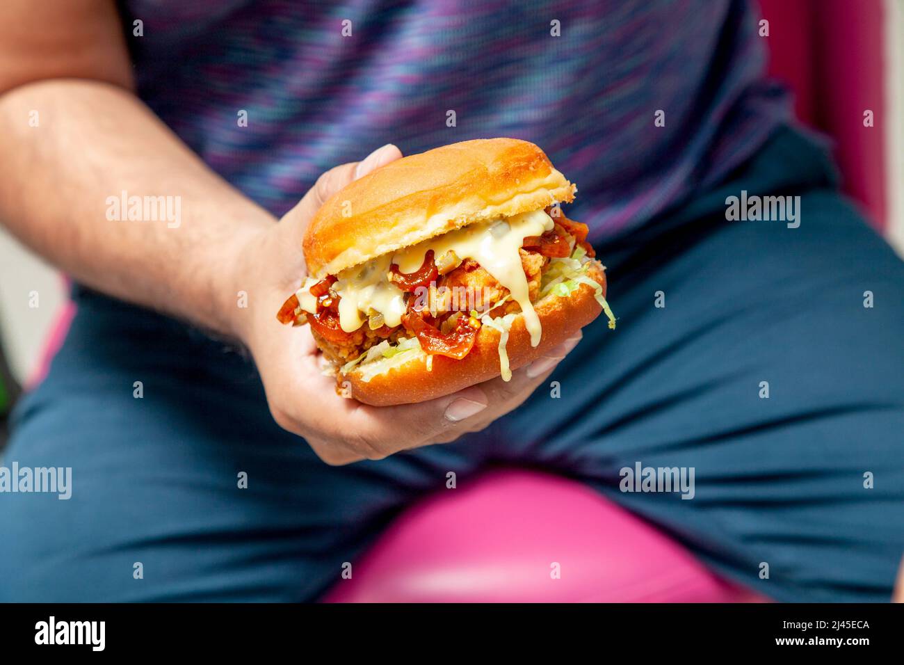 Mann mit einem würzigen gebratenen Hähnchenburger, der mit geschmolzenem Käse übergossen wird. Stockfoto
