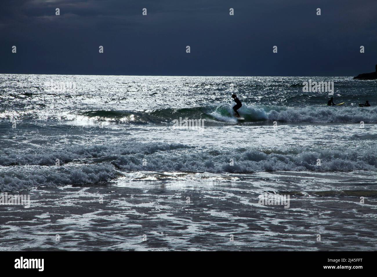 Silhouetten der Surfer Atlantischer Ozean im Praa Sands Cornwall, England kopieren den dunklen Himmel mit Wellen und silbrigem Meerwasser Kernow Stockfoto