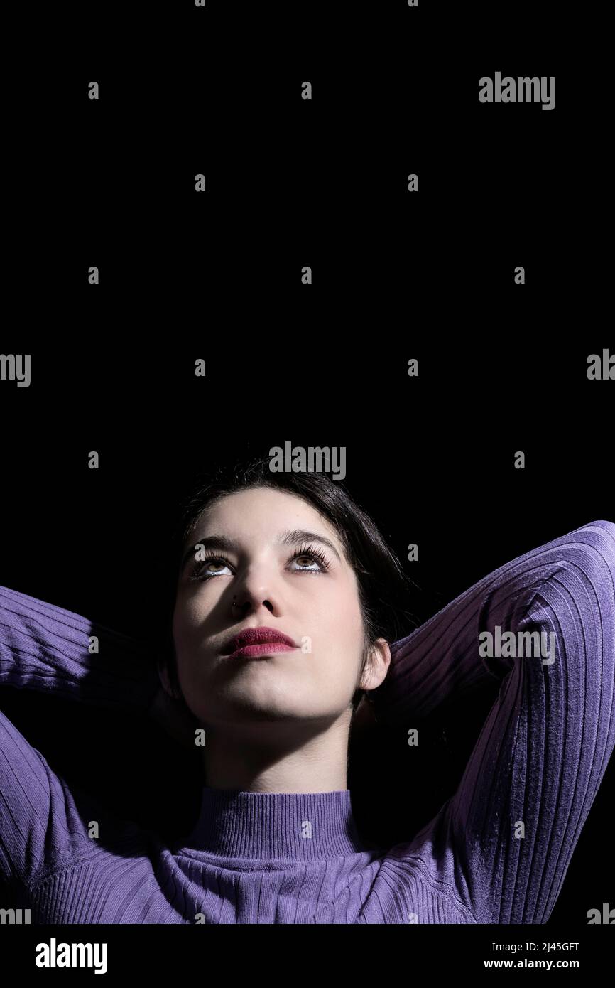 Brünette Frau mit Händen auf dem Kopf auf schwarzem Hintergrund Stockfoto
