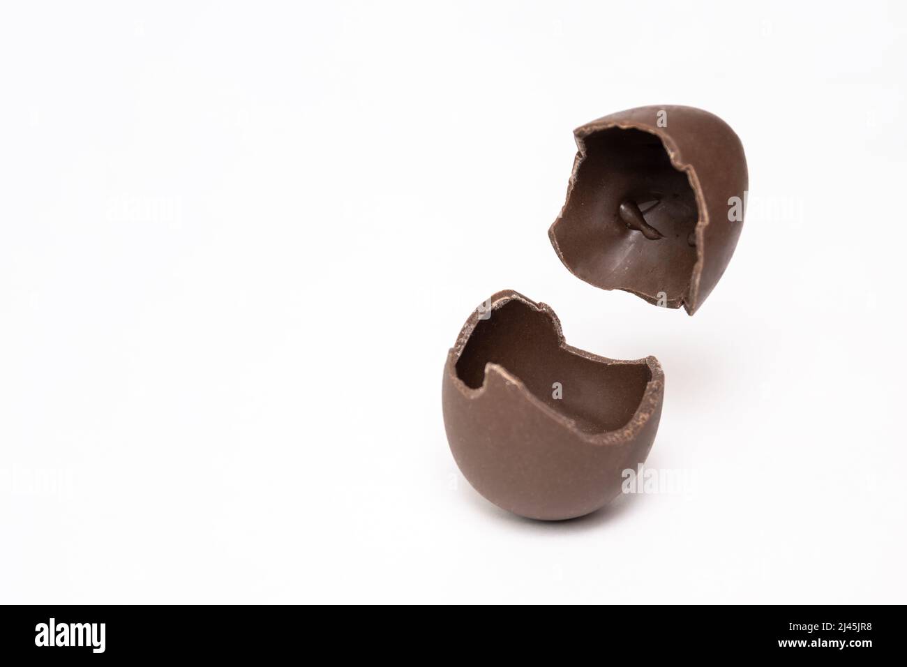 Geknackte Schokolade Osterei auf einem hellen Hintergrund, kopieren Raum. Ein zerbrochenes Milchschokoladenei mit fliegendem Deckel. Schokoladenoster-Konzept. Stockfoto