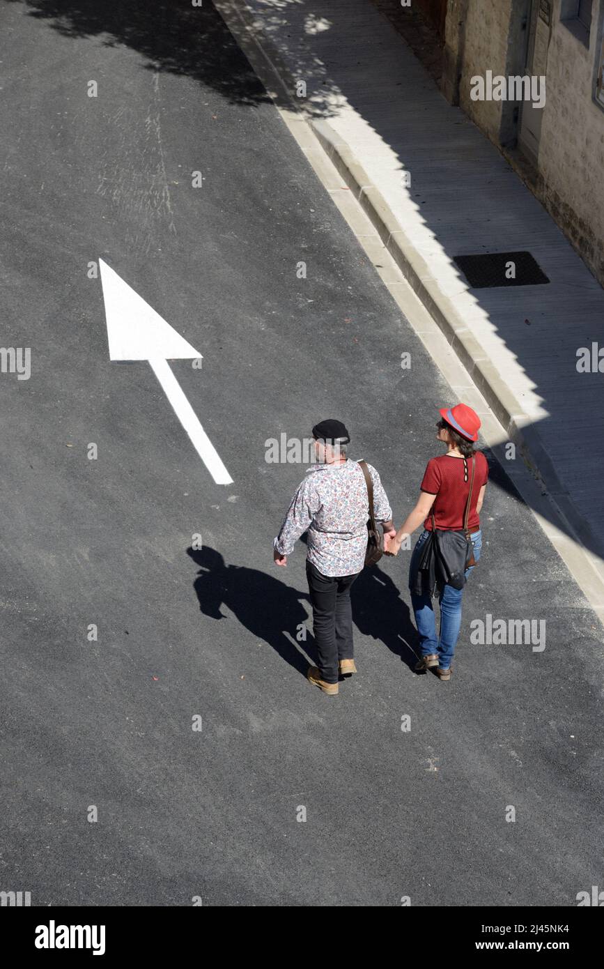 Touristikpaar Hände halten oder Hand in Hand gehen und Weißer Pfeil auf der Straße nach vorne zeigen Aigues-Mortes Gard Frankreich Stockfoto
