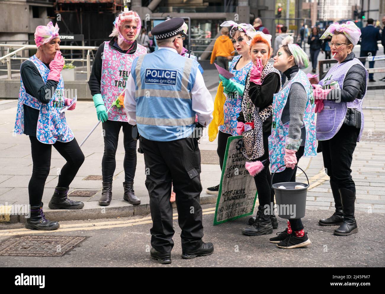 Aktivisten des Extinction Rebellion sprechen in Putzfrauen-Kleidung mit einem Polizeibeamten außerhalb von Lloyds of London in der City of London, während sie Lloyds dazu aufrufen, die Versicherung von Projekten für fossile Brennstoffe weltweit einzustellen. Bilddatum: Dienstag, 12. April 2022. Stockfoto