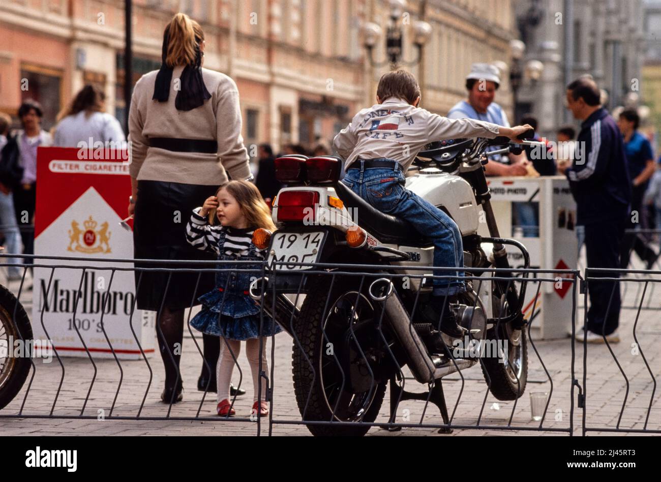 Ein kleiner Junge spielt auf einem Motorrad, das auf der Straße geparkt ist, Moskau, Russland, Mai 1990. Stockfoto