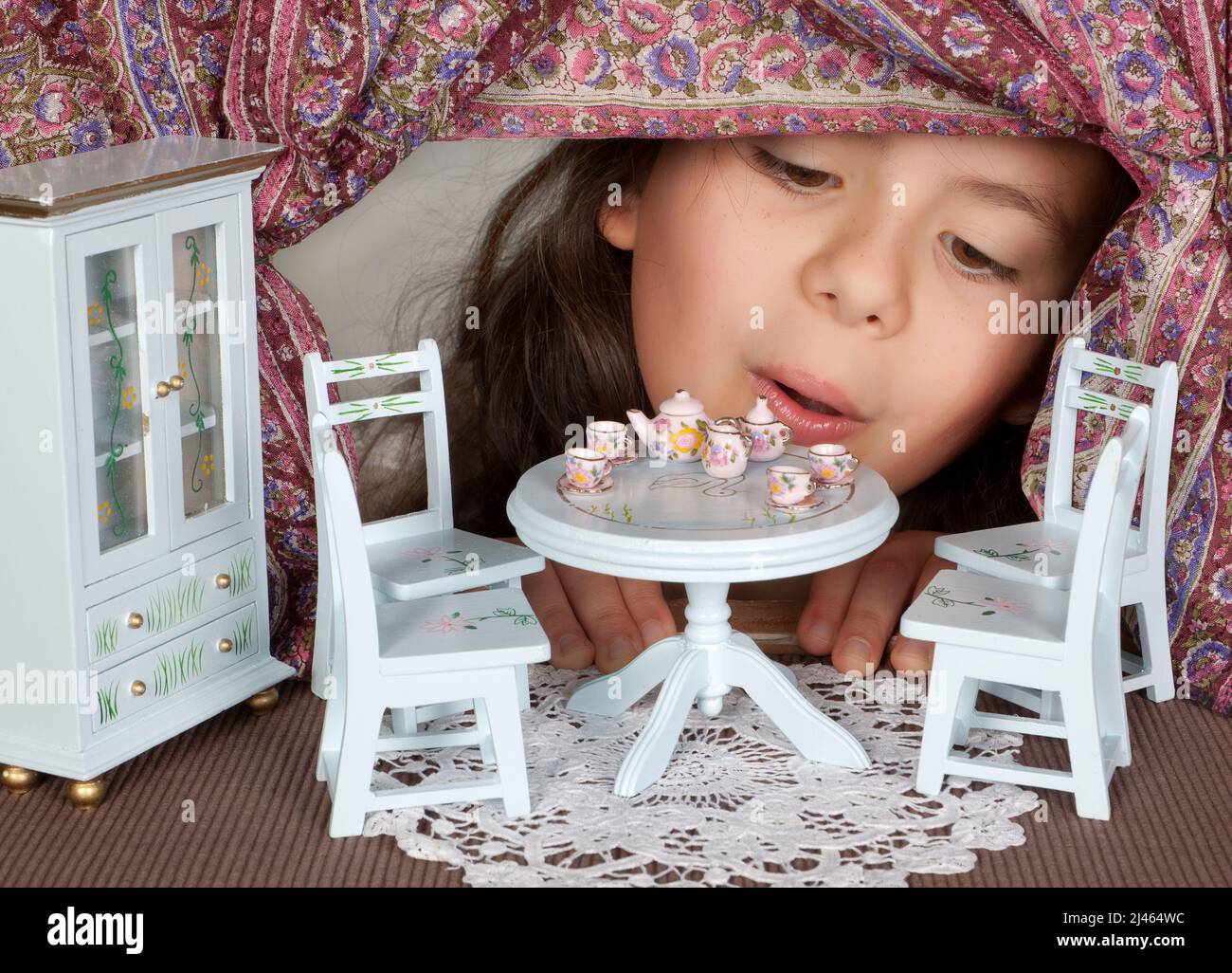 Kleines Mädchen, das durch ein Fenster in ein Puppenhaus blickt wie in alice im Wunderland Stockfoto