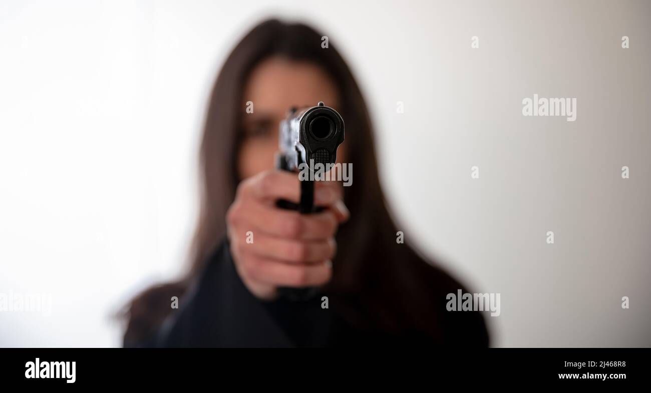 Frau, die ein Gewehr in der Hand hält und auf die Kamera zeigt. Weibliche Geheimagentin, Killer oder Spion dunkel lange Haare, kopieren Raum. Selektiver Fokus Stockfoto