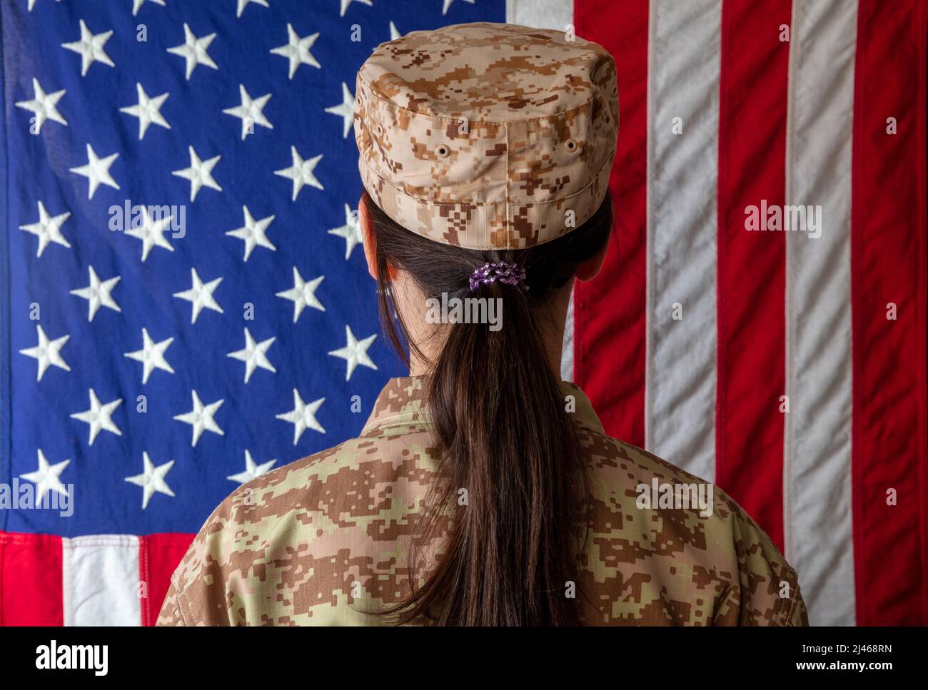 Soldatin der US-Armee, die vor einer amerikanischen Flagge steht. Frau in Militäruniform Rückansicht Stockfoto