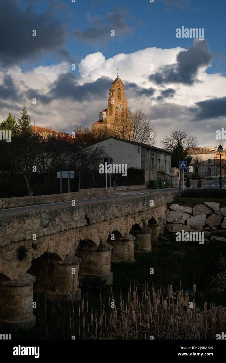 Katholische Kirche - Parroquia de la Asuncion de Nuestra Senora - in Venialbo, in der Nähe von Zamora, Spanien. Gesehen über der alten Steinbrücke über Arroyo Talanda Stockfoto