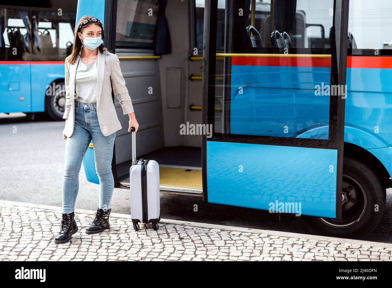 Eine junge Frau mit Maske und Gepäck hat gerade nach einer langen Reise den Bus verlassen Stockfoto