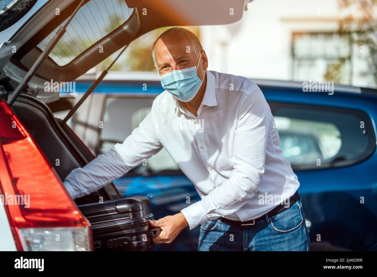 Ein Taxi- oder Uber-Fahrer, der das Gepäck aus dem Kofferraum seines Autos entlädt Stockfoto