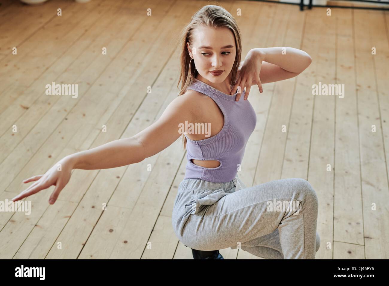 Liebenswürdiges Teenager-Mädchen in aktivem Ausstreckarm während der Ausübung während Mode Tanz-Training auf Holzboden des modernen Studios Stockfoto