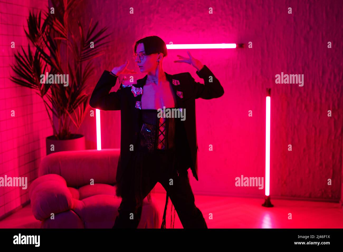Moderne junge Tänzerin in eleganter Kleidung, die im Nachtclub modischen Tanz aufführt, während sie im Zimmer oder Studio mit pinkem Neonlicht steht Stockfoto