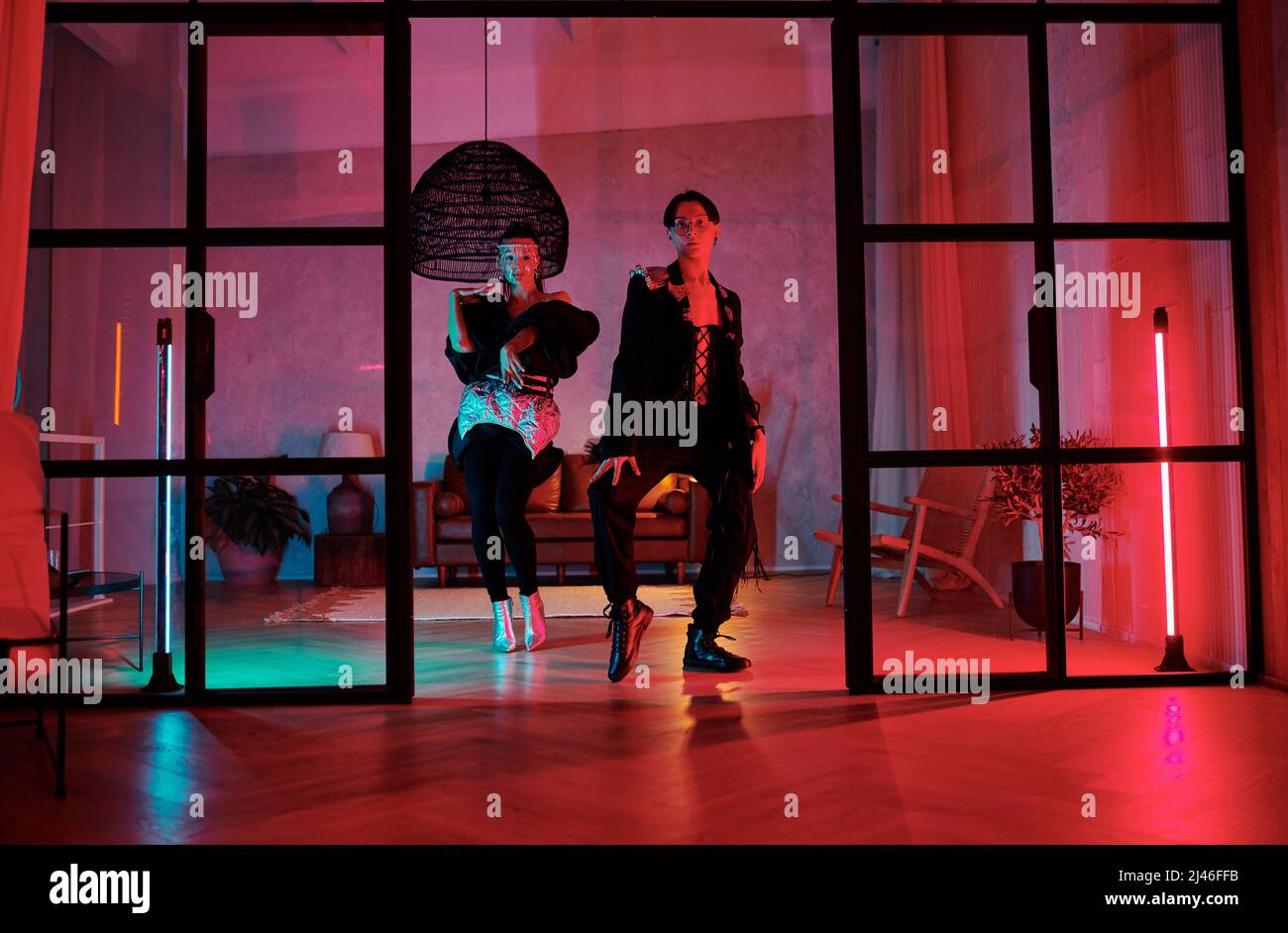 Zwei Jugendliche dynamische Tänzer, die im Studio oder Loft-Apartment mit pinken Neonlampen vor der Tür modische Tanzbewegungen aufführen Stockfoto