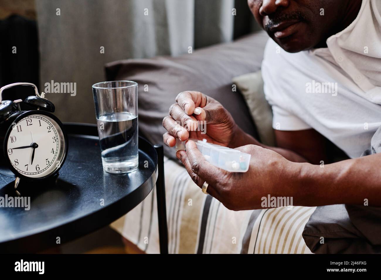 Hände eines zeitgenössischen älteren schwarzen Mannes, der am Morgen nach dem Schlaf lange Plastikbehälter mit Pillen hielt, während er Medikamente einnahm Stockfoto