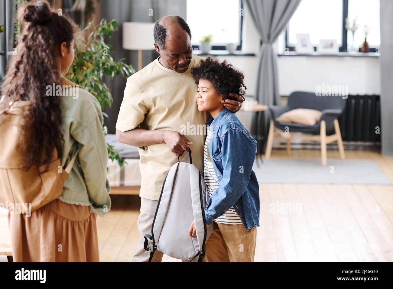 Pensionierter schwarzer Mann, der niedlichen Enkel schätzt, während er seinen Schulrucksack hält und ihn beim Besuch von Enkelkindern ansieht Stockfoto