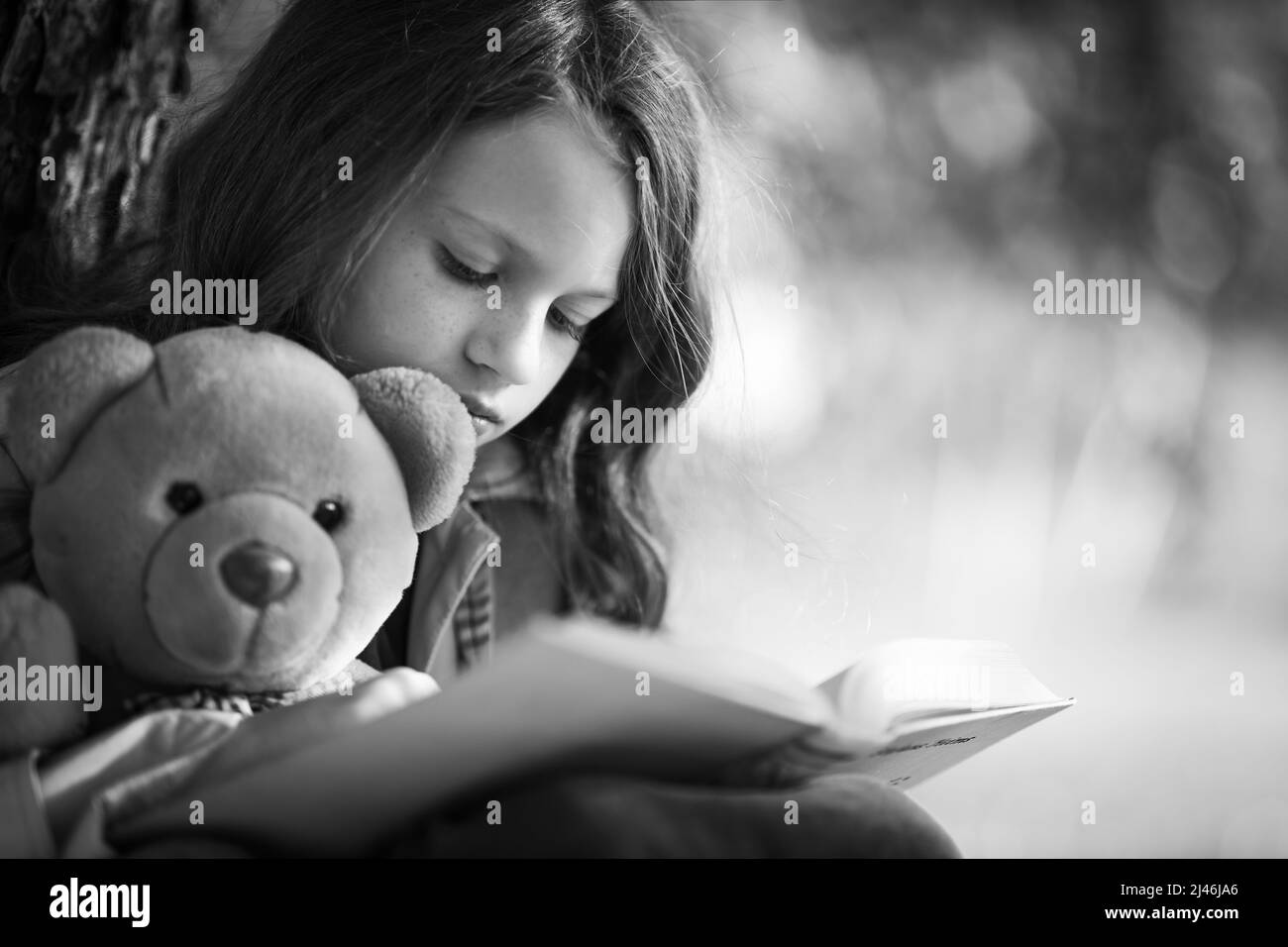 Das Mädchen liest ein Märchenbuch mit einem Teddybär. Stockfoto