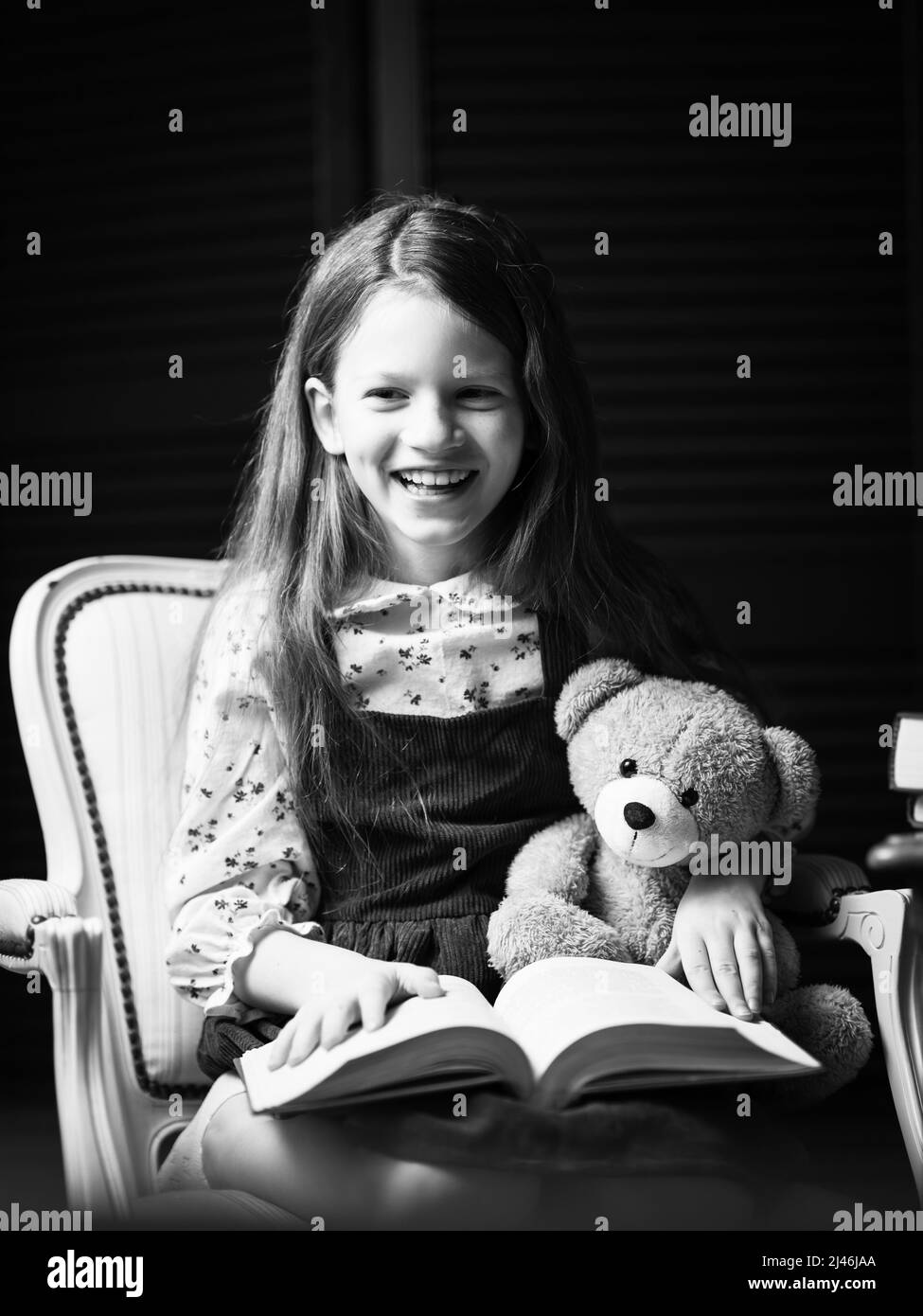 Ein glückliches Mädchen liest eine lustige Geschichte mit einem Teddybär. Stockfoto
