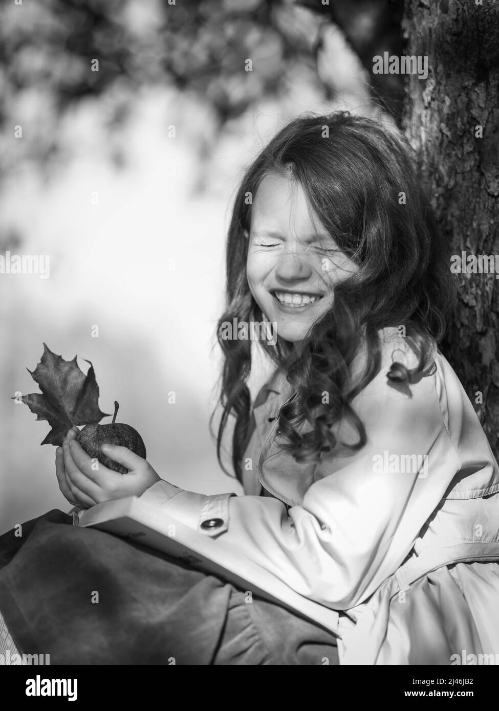 Ein glückliches Mädchen im Park mit einem Buch und einem Apfel in den Händen. Stockfoto