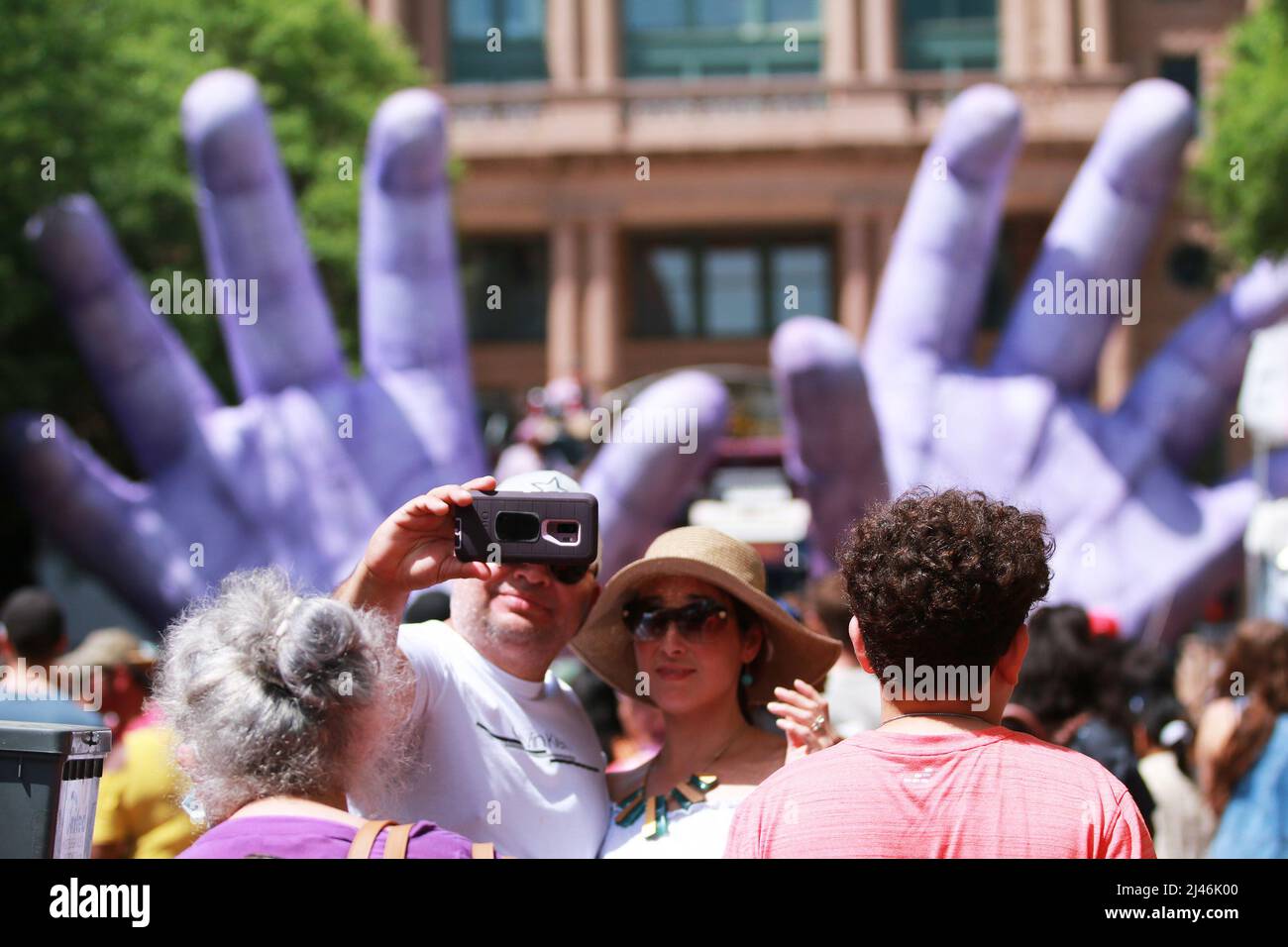 Fort Worth, Texas, USA. 10. April 2022. Ein Paar macht während des Main Street Fort Worth Arts Festivals ein Selfie vor Squonks visueller Extravaganz namens „Hand in Hand“. Zwei riesige, lila Puppenhände, die so entworfen wurden, dass das Publikum die Takelage ergreifen und an der Show am 10. April 2022 teilnehmen kann. (Bild: © Javier Vicencio/ZUMA Press Wire) Stockfoto