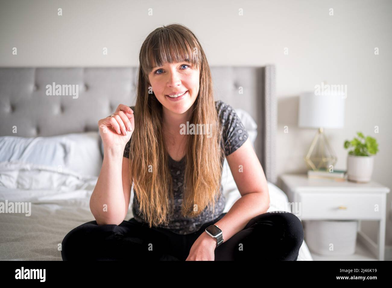Kaukasische Frau mit braunem Haar und Pony sitzt auf einem Bett Stockfoto