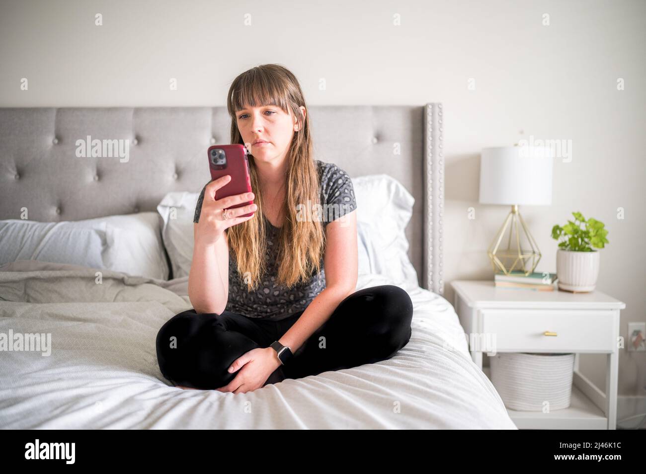 Frau, die auf dem Bett sitzt und auf das Telefon schaut Stockfoto
