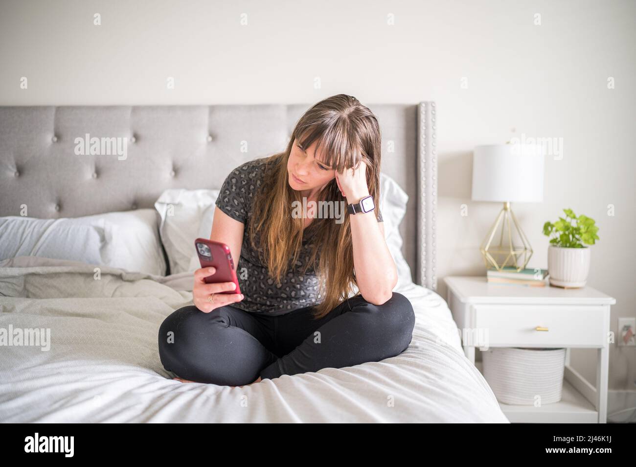Frau, die auf dem Bett sitzt, während sie auf ihrem Telefon scrollt Stockfoto