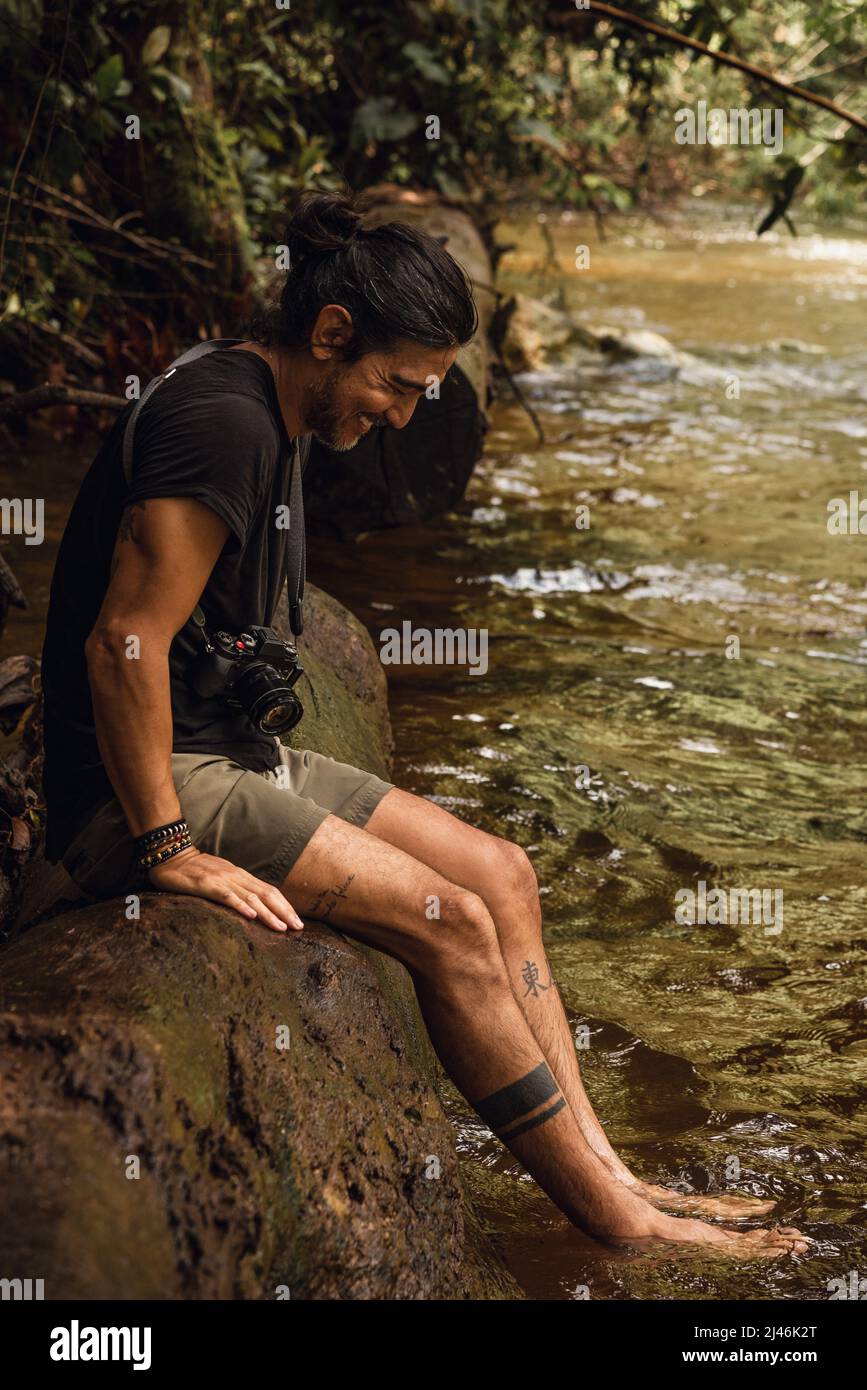 Mann sitzt auf einem Baum mit seinen Füßen auf dem Fluss Stockfoto