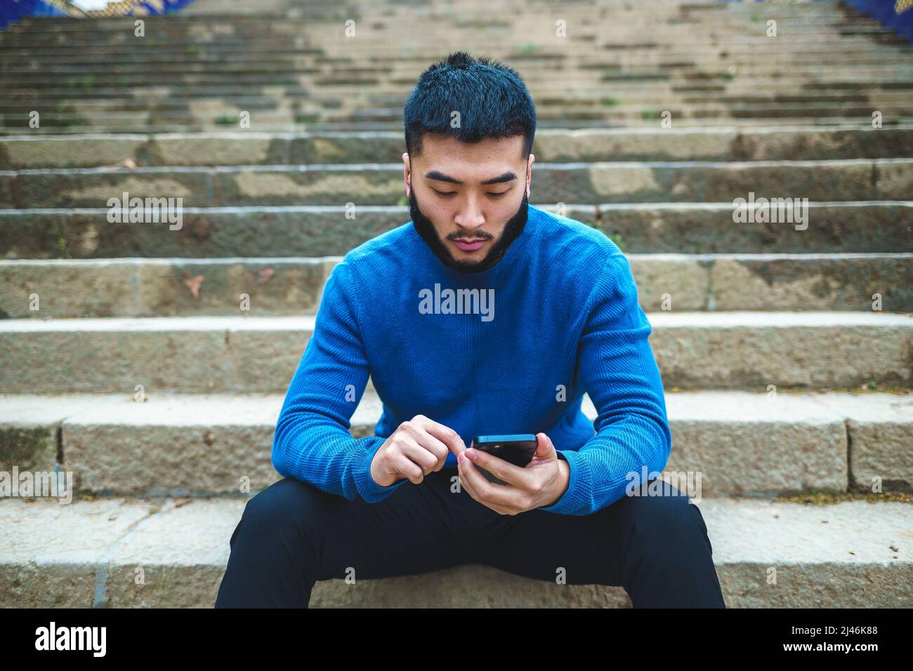 Seriöser ethnischer Mann, der Smartphone auf Steintreppen benutzt Stockfoto