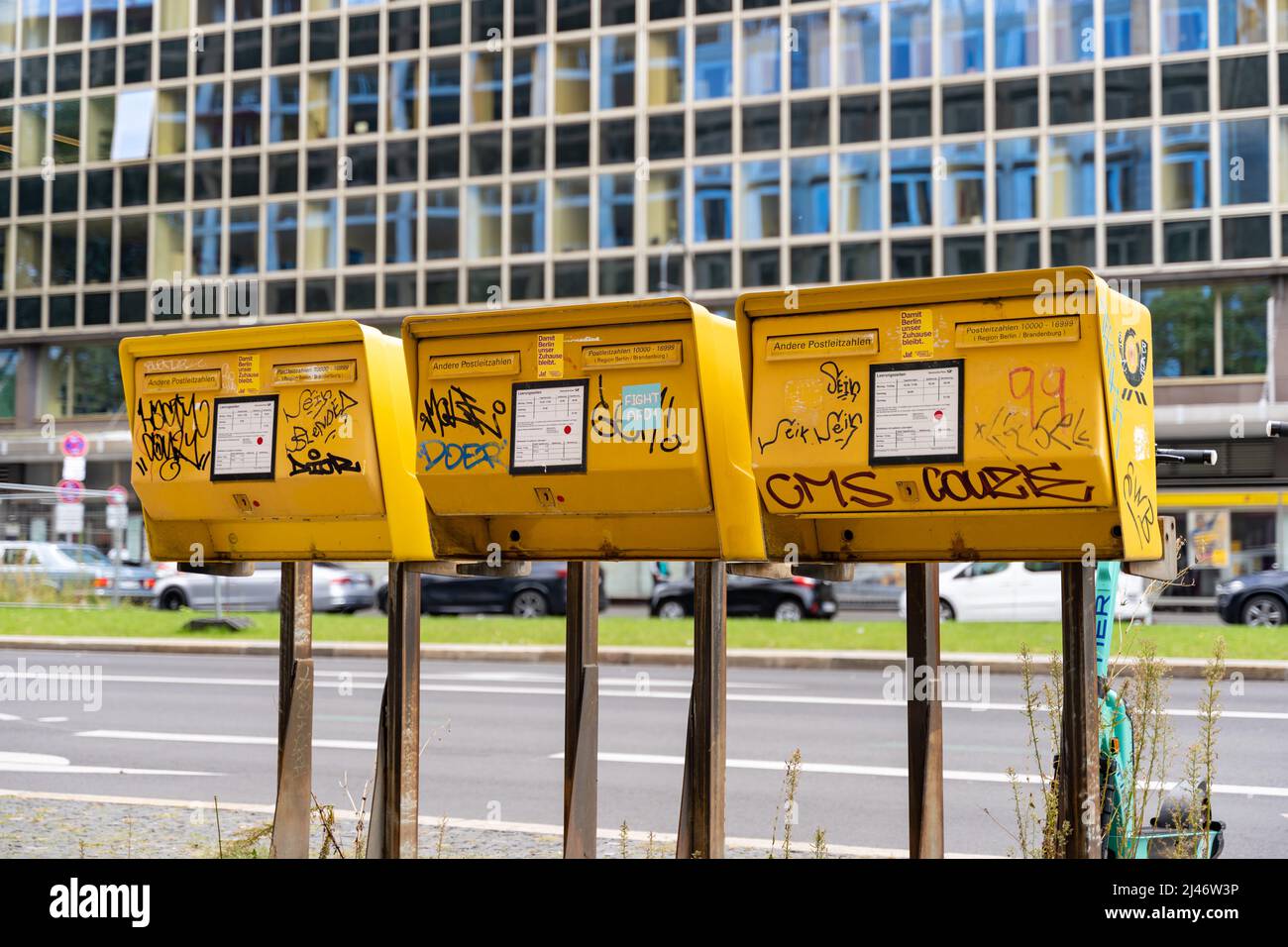 Drei gelbe Briefkästen der Deutschen Post an einer großen Straße in der Stadt. Postfächer zum Senden von Briefen und Karten. Graffiti-Tags und Aufkleber. Stockfoto