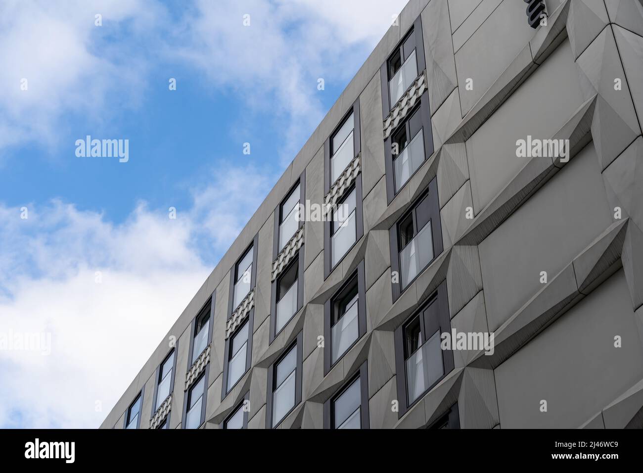 Modernes Fassadendesign vor einem blauen Himmel mit weißen Wolken. Graue Elemente mit Relief und Glasfenstern. Futuristische Architektur im Außenbereich. Stockfoto