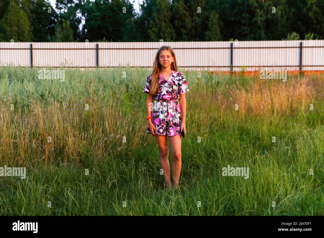 Defocus schöne lächelnde Teenager-Mädchen im Kleid stehen vor grünen Sommer Hintergrund. Hohes Mädchen 12 oder 13 Jahre alt auf Sommerrasen. Nicht fokussiert. Stockfoto