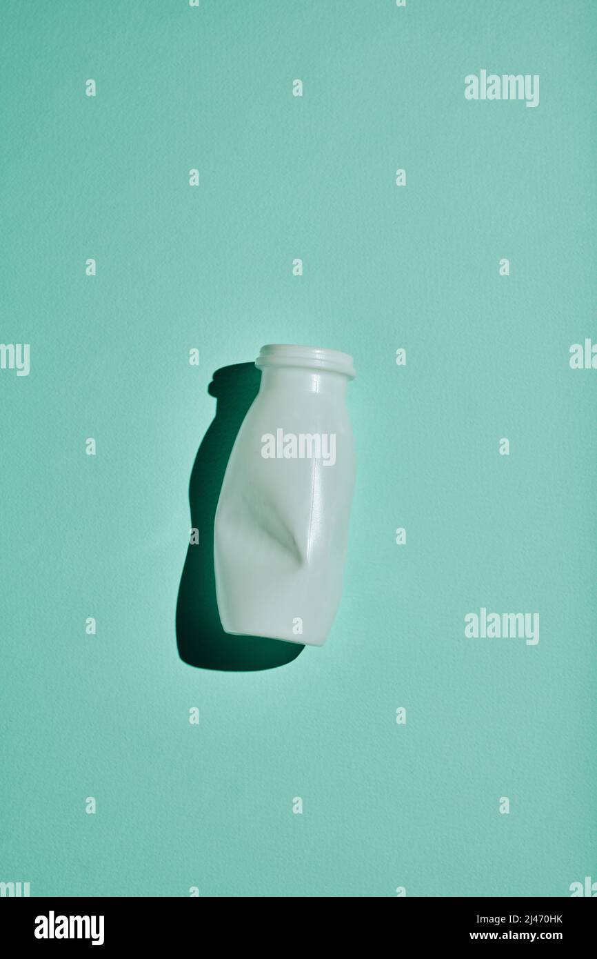 Vertikale, minimalistische, flache Aufnahme einer weißen Plastikflasche auf blaugrünem Hintergrund, bewusstes Konsum- und Recyclingkonzept Stockfoto