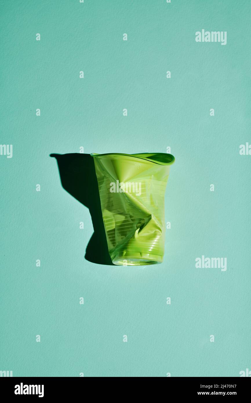 Vertikale moderne flache Lage Schuss von zerknittert grünen Kunststoff-Tasse auf hellblaugrünem Hintergrund, bewussten Verbrauch und Recycling-Konzept Stockfoto
