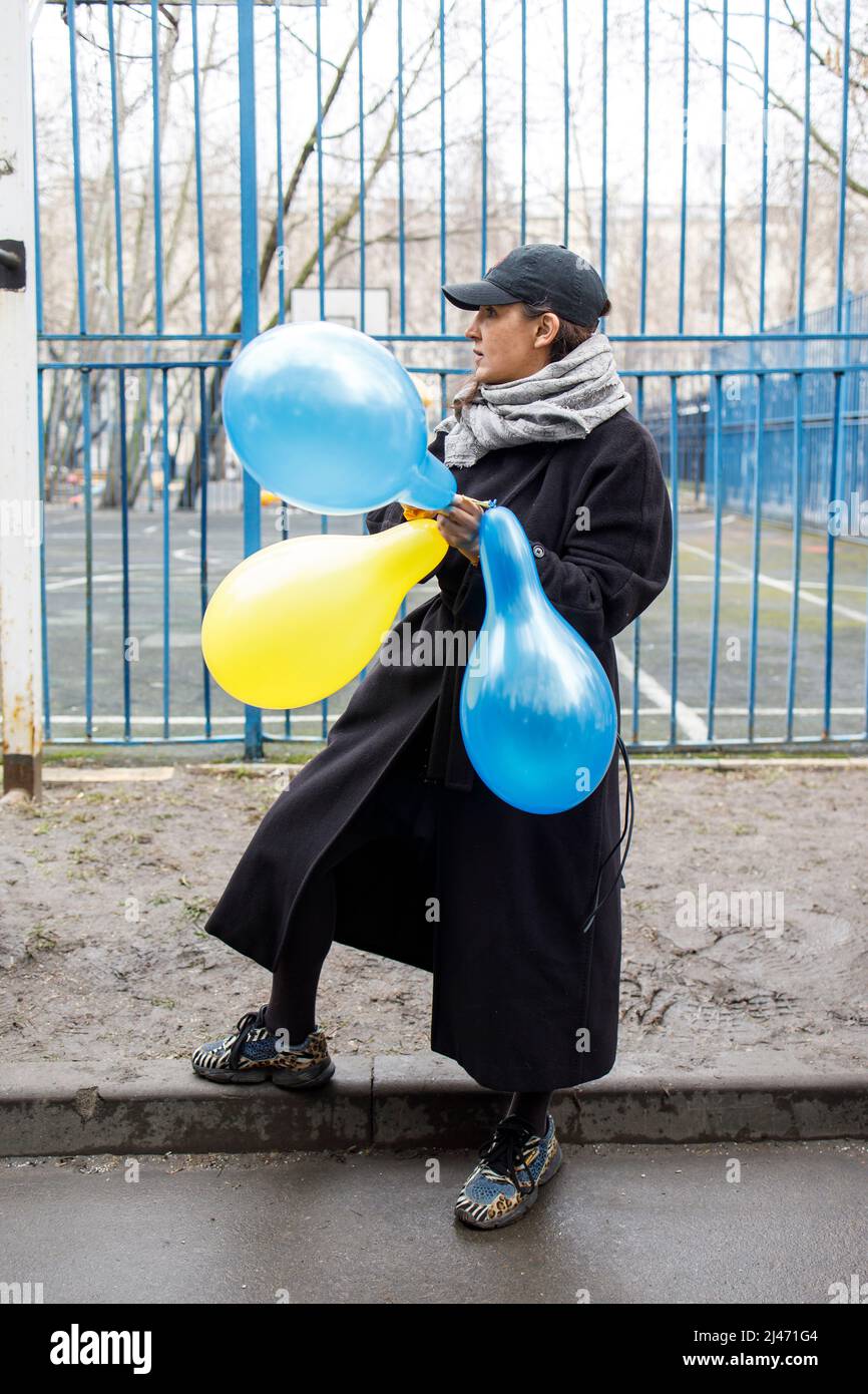 Moskau, Russland - am 12. April 2022 kamen Menschen vor Gericht, um die verhafteten Studenten im Fall Doxa zu unterstützen. Eine Frau bläst gelbe und blaue Luftballons auf Stockfoto